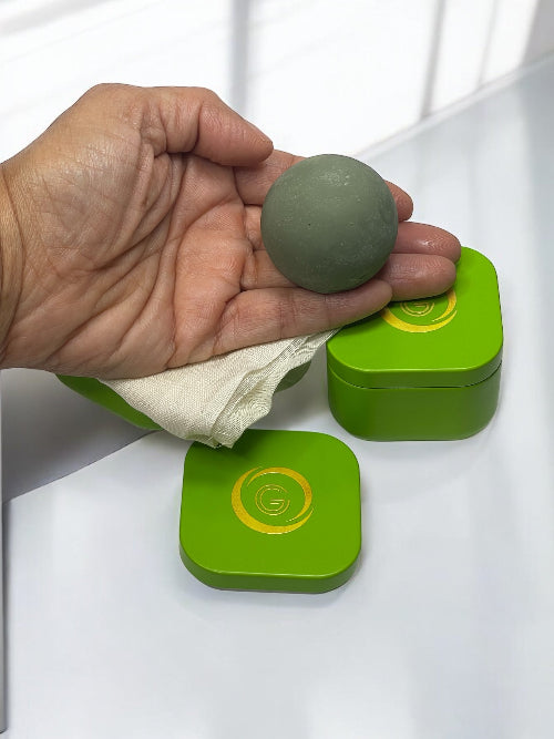 Hand holding a green ball above two green containers with yellow lids on a white surface.
