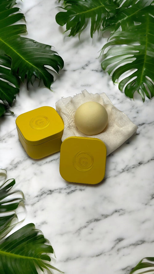 Yellow containers with a round beige object on a marble surface with green leaves.