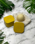 Yellow containers with a round beige object on a marble surface with green leaves.