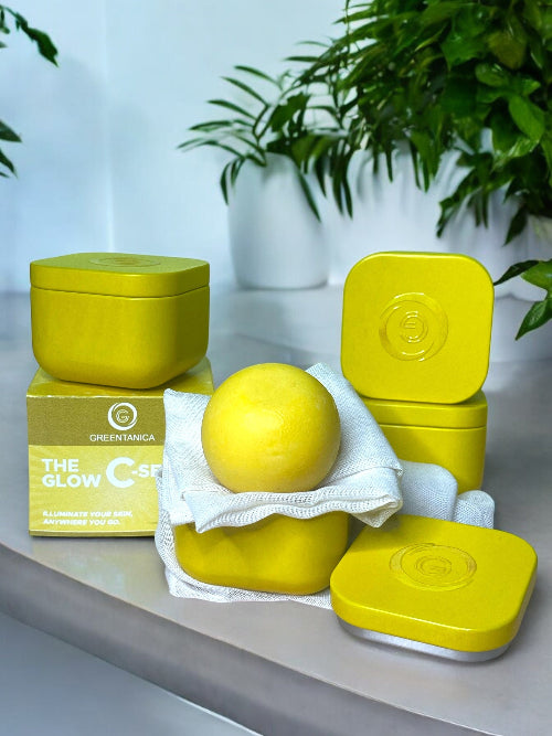 Yellow skincare product set with containers and a ball on a light surface with greenery in the background.