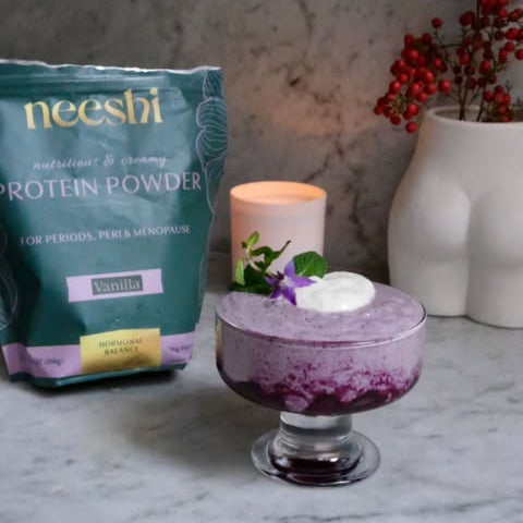 Neeshi protein powder package with a purple dessert and candle on a marble surface.