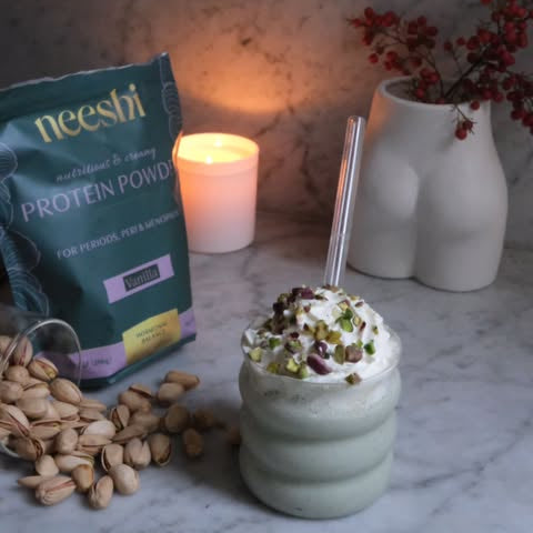 Protein shake with pistachios and neeshi protein powder package on a marble surface.