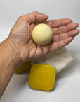 Hand holding a beige ball with a yellow container in the background