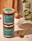 Neeshi dark cacao spread jars on a wooden surface with a dessert and spoon.