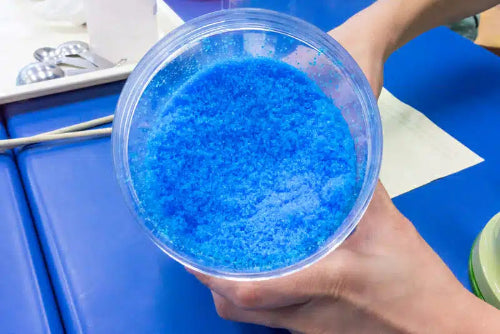 Hand holding a container of blue crystals in a kitchen setting