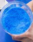 Hand holding a container of blue crystals in a kitchen setting