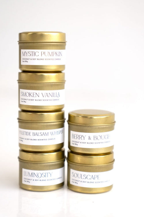 A set of six travel-size candles from Pivotal Moments, with labels showing various scents like Mystic, Broken, Balsam, and Berry. Each candle is in a gold tin with white label branding.