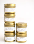 A set of six travel-size candles from Pivotal Moments, with labels showing various scents like Mystic, Broken, Balsam, and Berry. Each candle is in a gold tin with white label branding.