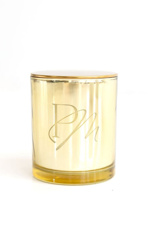A gold tin candle with a clear wax top, embossed with the initials 'P M'.