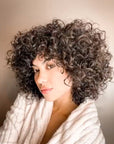 Woman with curly hair wearing a white scarf against a neutral background