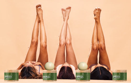 Three women with their legs up, showing smooth skin, with Harmony Skincare products in front.