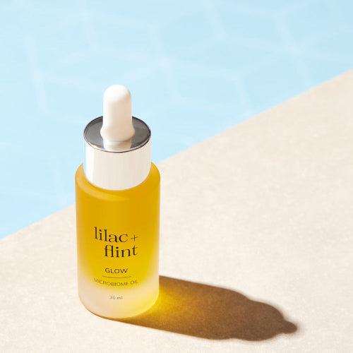 Yellow skincare dropper bottle labeled 'lilac + flint' on a light blue and beige background