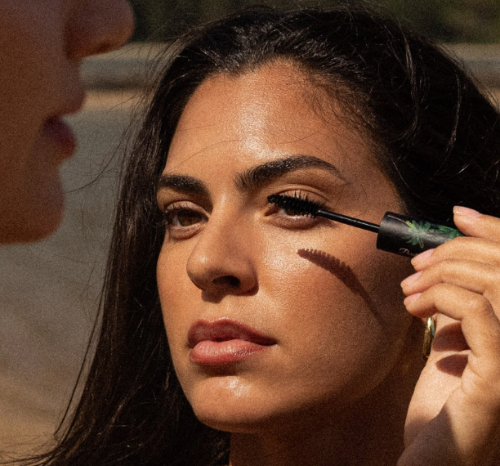 Woman applying mascara with a brush to another person's eyelashes.