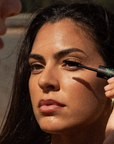 Woman applying mascara with a brush to another person's eyelashes.