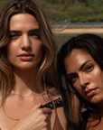 Two women standing close to each other outdoors with a natural background