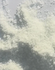 A close-up view of a light off-white crystalline powder or salt granules scattered on a pale gray surface.