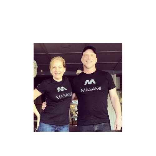 A man and a woman standing and posing in front of a camera, both wearing black T-shirts with the 'MASAMI' brand logo on the front.