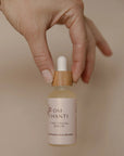 Hand holding a bottle of 'OM Chanti Time Travel Serum' against a beige background