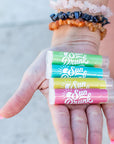 Hand holding a set of colorful sunblock sticks with text on a blurred background