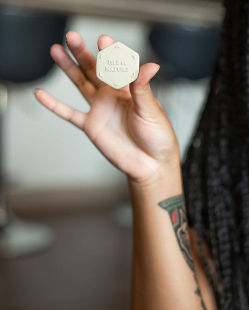 A hand holding a small hexagonal ceramic scent coin with the text 'PAGUA BAY' on it, with a blurred background.