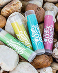 Colorful lip balms with 'Sun & Fun' branding on a bed of rocks.