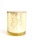 A gold tin candle with a clear wax top, embossed with the initials 'P M'.
