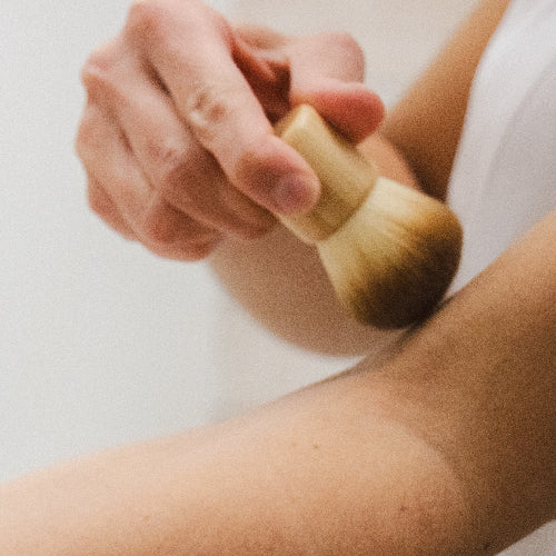 Person applying a cosmetic product with a brush on a plain background