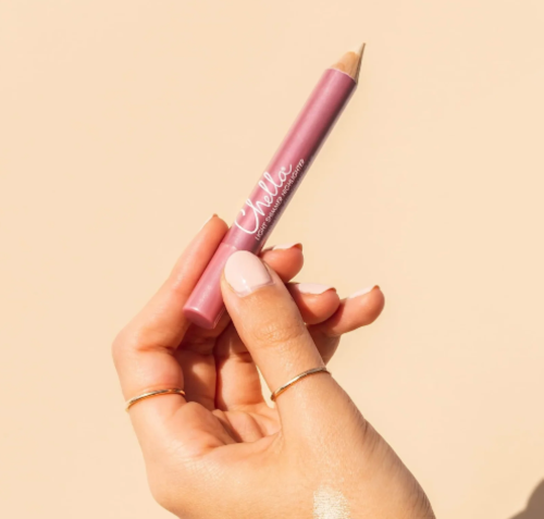 A hand holding a pink makeup pencil with the brand name 'Chellie' visible on the barrel, set against a solid beige background.
