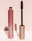 Chelle Cosmetics Good Skin Lip Colour in a metallic rose pink tube, shown next to its wand applicator on a light pink glittery background.