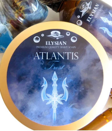 A round tin of Elysian Atlantis Frost premium quality shave soaps, featuring a blue and white icy design with a glowing trident logo and a gold-colored rim.
