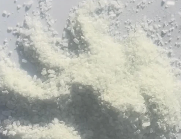 A close-up view of a light off-white crystalline powder or salt granules scattered on a pale gray surface.