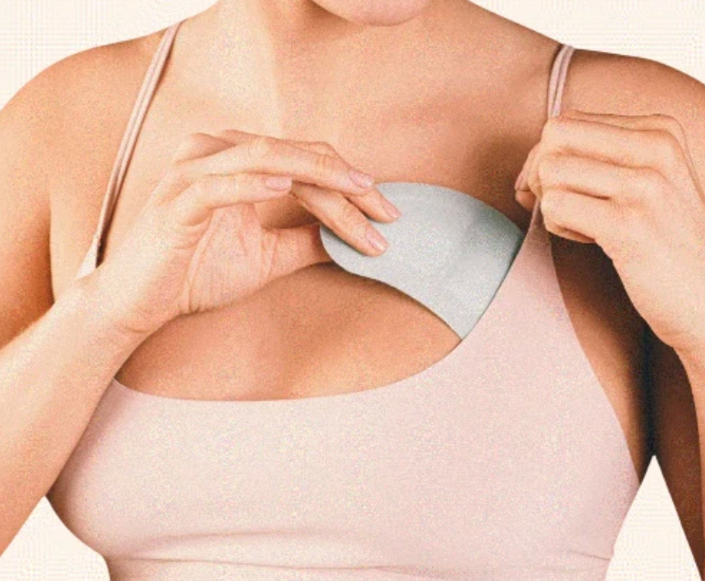 A close-up of a woman wearing a light beige camisole top and adjusting a light gray underwire bra cup.
