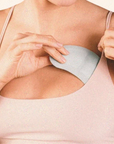 A close-up of a woman wearing a light beige camisole top and adjusting a light gray underwire bra cup.