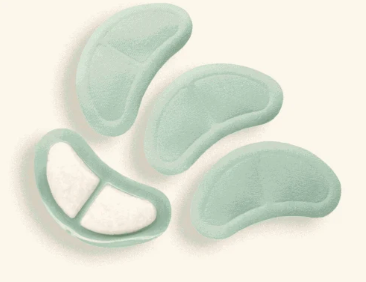 Four pale mint green adhesive pads or patches arranged on a light cream background, with one pad shown split open to reveal a white inner layer.