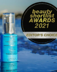Viking Beauty Organic Sunscreen Night Cream bottle in a bright blue bottle with a silver pump, shown next to a black circular badge that reads 'beauty shortlist AWARDS 2021 EDITOR'S CHOICE'. The background is a blurred blue water scene.
