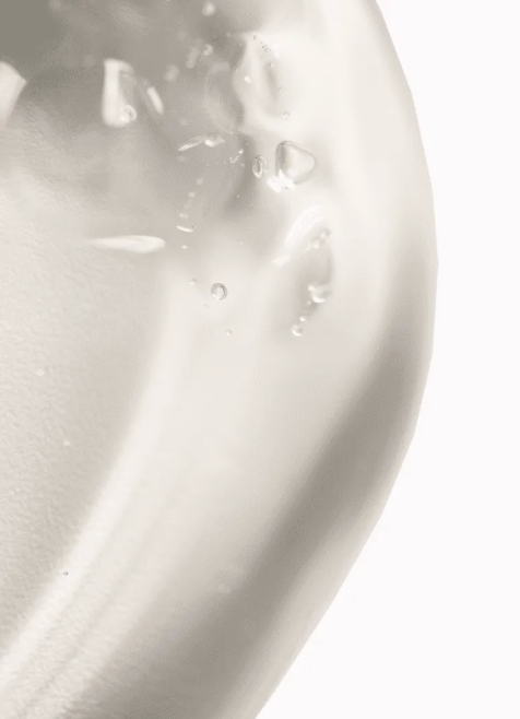 A close-up of a smooth, glossy white cosmetic cream or gel texture with small water droplets on a clean white background.