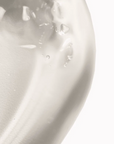 A close-up of a smooth, glossy white cosmetic cream or gel texture with small water droplets on a clean white background.