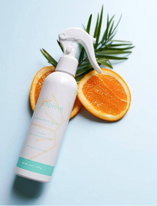 A bottle of Espieve Revive Body Spray with a white trigger sprayer, styled with sliced oranges and green palm leaves on a light blue background.