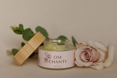 Jar of 'OM Chanti' product with a wooden lid and pink rose on a neutral background