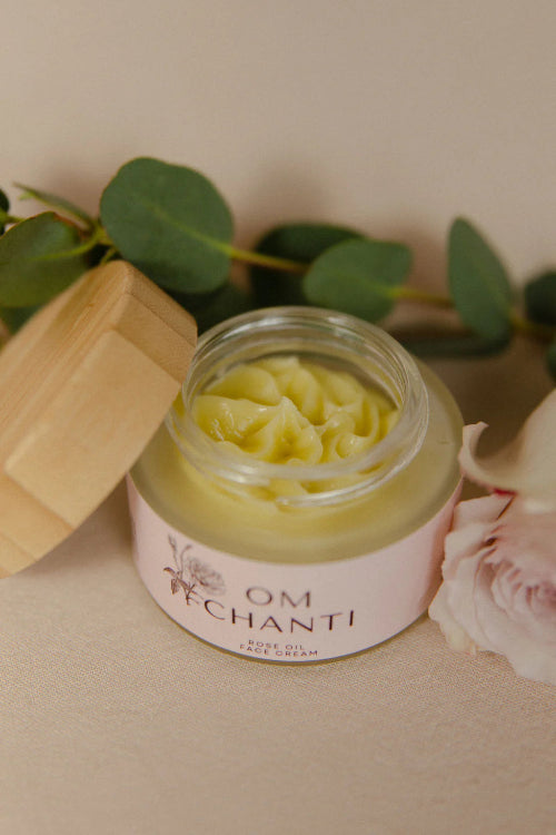Jar of cream with a wooden lid on a light surface with green leaves in the background