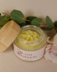 Jar of cream with a wooden lid on a light surface with green leaves in the background
