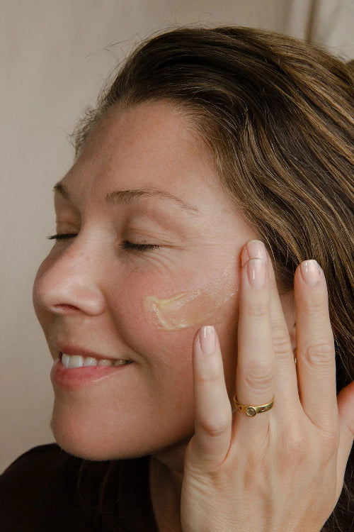 Woman applying cream to her face with a neutral background
