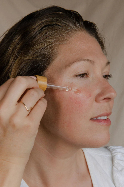 Woman applying a skincare product with a dropper to her face.