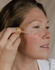 Woman applying a skincare product with a dropper to her face.