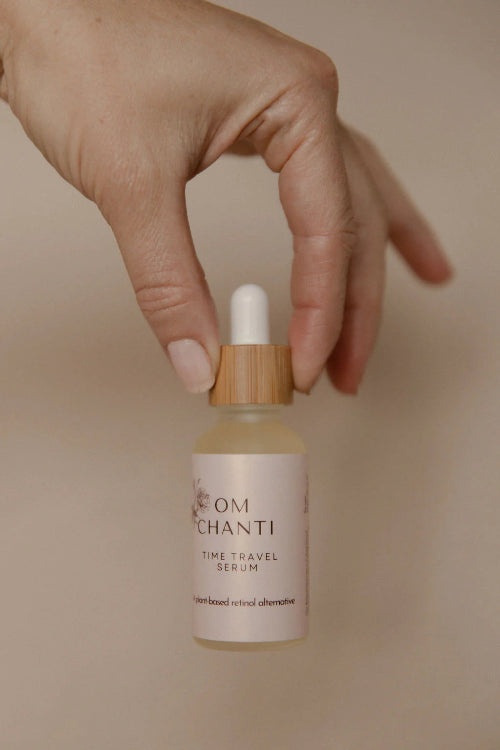 Hand holding a bottle of 'OM Chanti Time Travel Serum' against a beige background