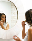 Woman applying makeup in front of a round mirror.